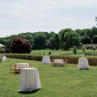 Round hightop tables with white linen tablecloths on grass in scenic country setting
