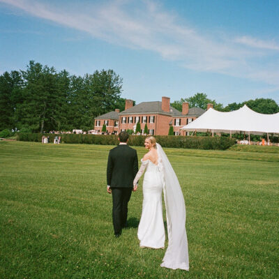 Bride and groom walking on grass towards Georgian estate with tented reception