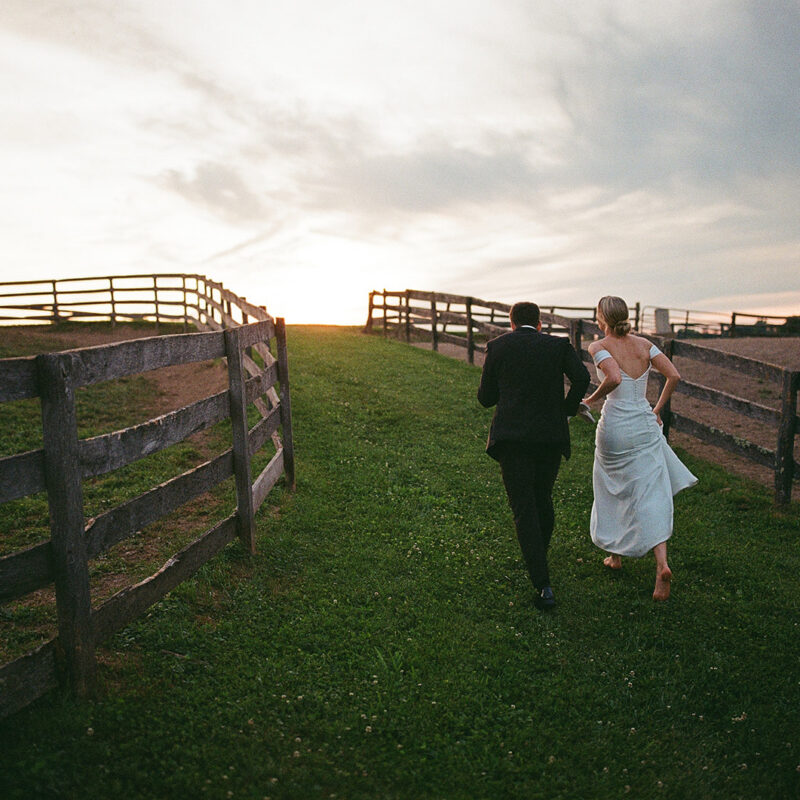 Bride and groom running near fence line at twilights