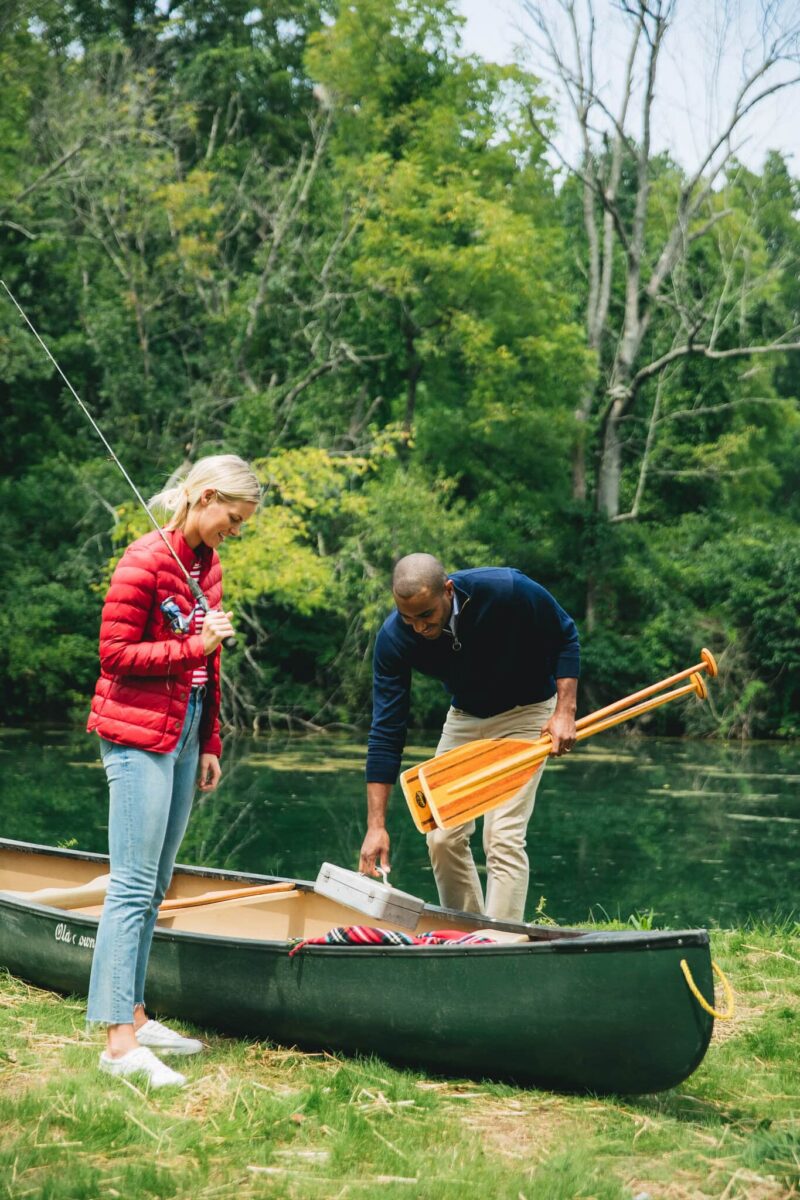 Two guests loading a canoe at the water's edge, one holding paddles and one with a fishing rod