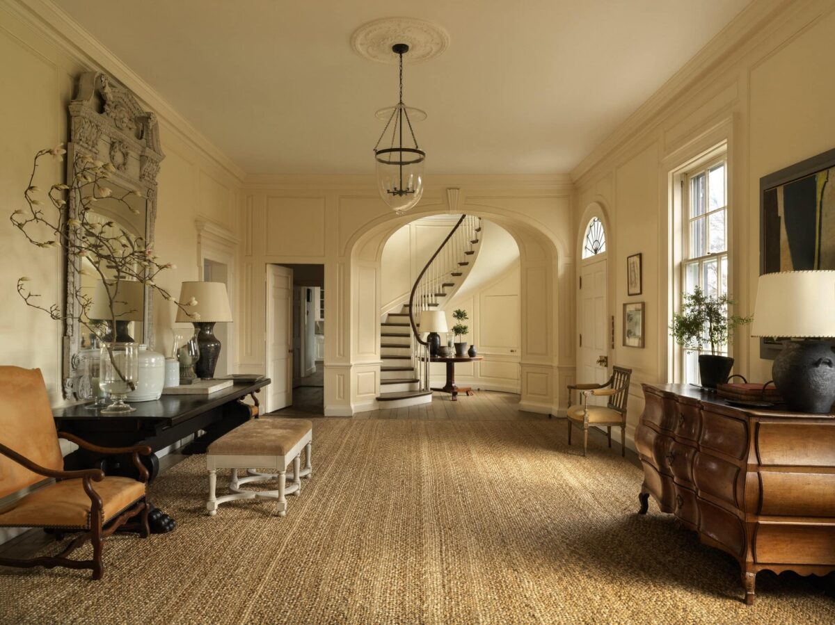 The manor entry hall, with a curved staircase, carved overmantel mirror and glass lantern