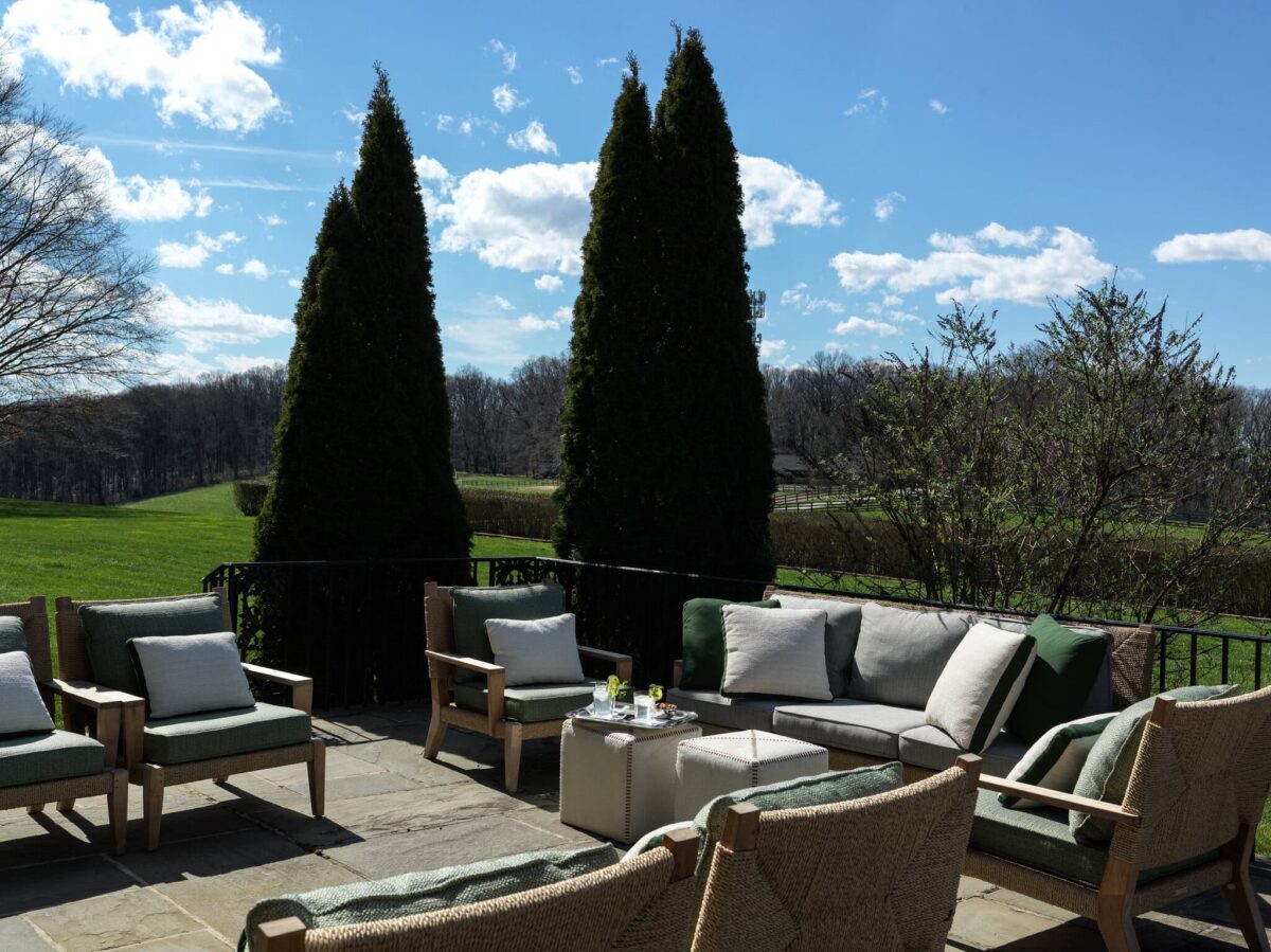 The stone terrace set with cushioned seating, framed by tall evergreens with open pasture beyond