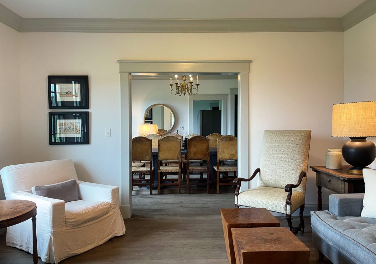 A sitting room looking through wide doors to the dining room, with hide-backed chairs and a brass chandelier