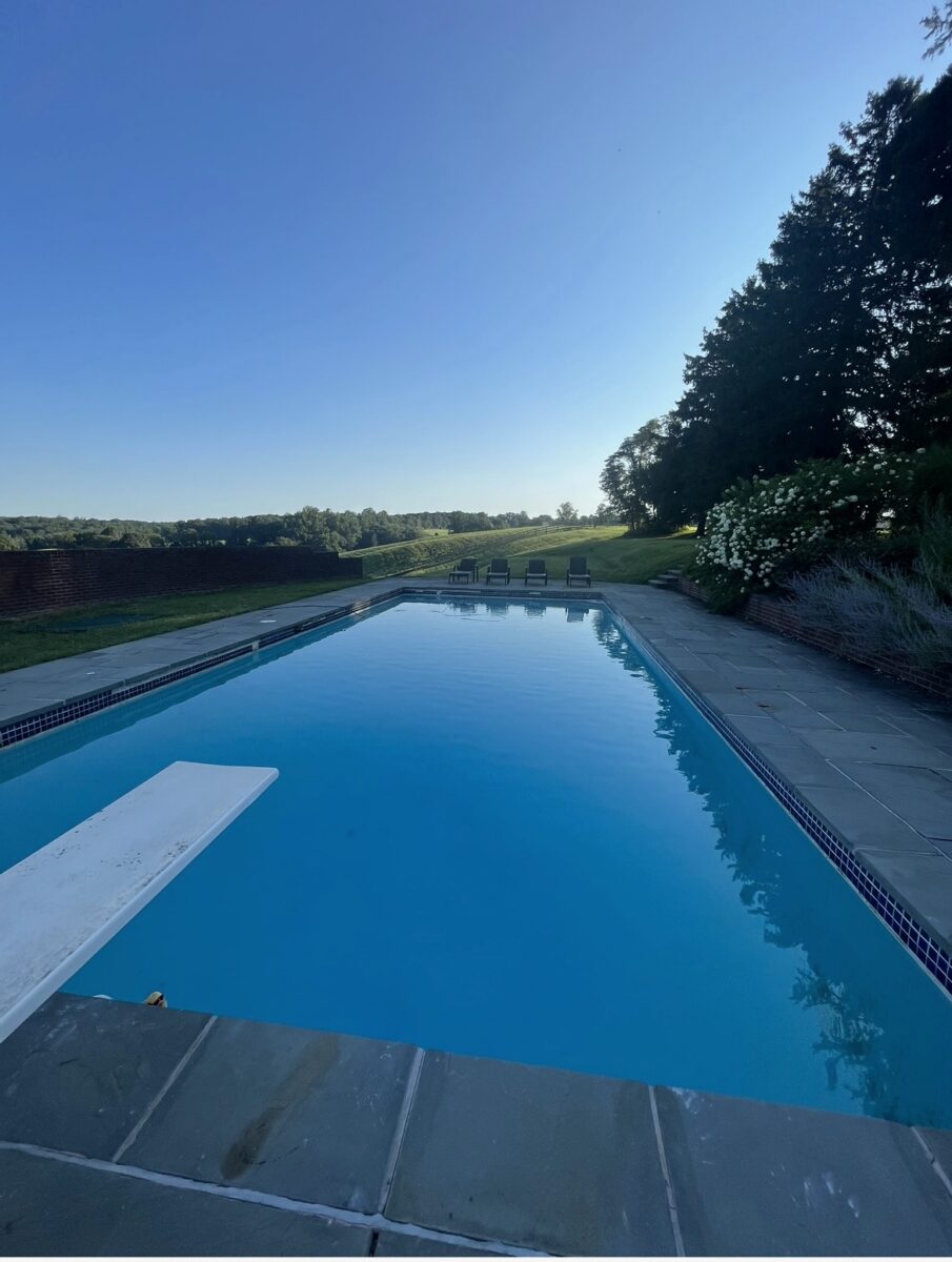 The swimming pool with a diving board and bluestone surround, set against a brick wall and open fields