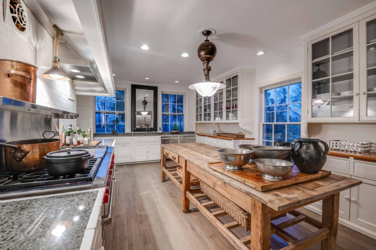 The kitchen at dusk, with a professional range, copper pots and a long reclaimed-wood work table