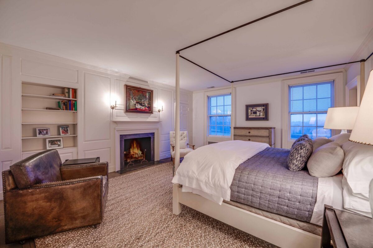 Guest bedroom with a four-poster bed, a lit fireplace and windows looking out over the fields