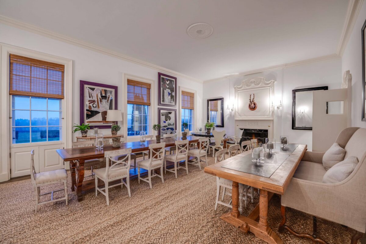 The dining room laid for a seated dinner on two long tables, with a fire lit and windows over the fields