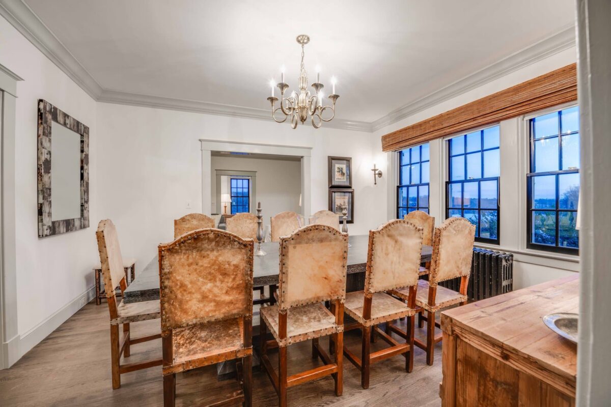 A dining room with a long table, hide-backed chairs and windows looking out over the countryside