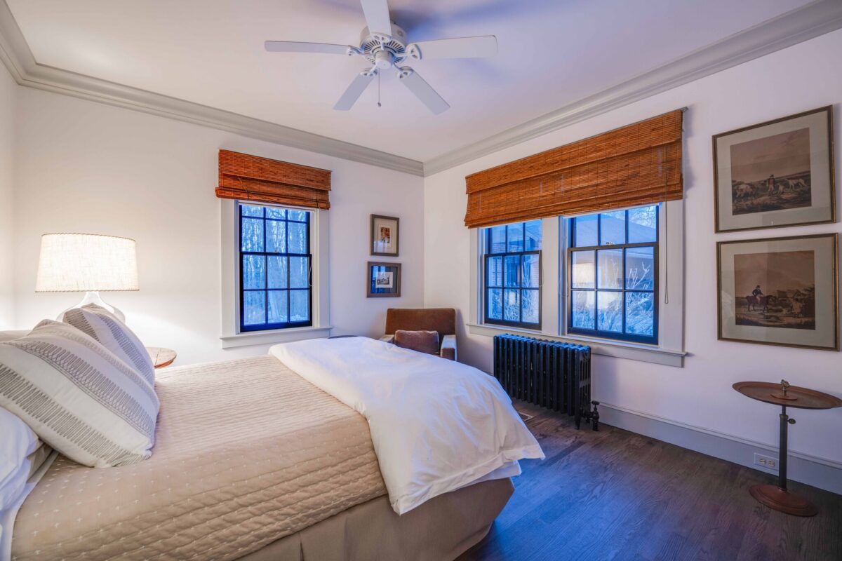 A guest bedroom with pale quilted bedding, sporting prints and shuttered windows onto the trees