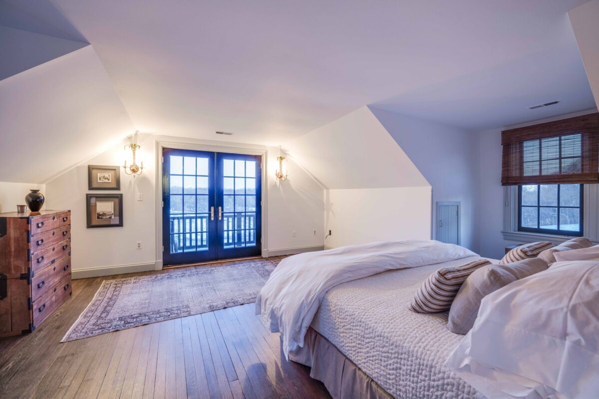 An upstairs bedroom under the eaves, with French doors opening onto a balcony above the fields