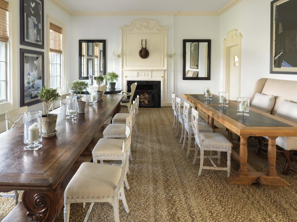 Two long tables set for a seated dinner in the dining room, with candles, topiaries and a fireplace